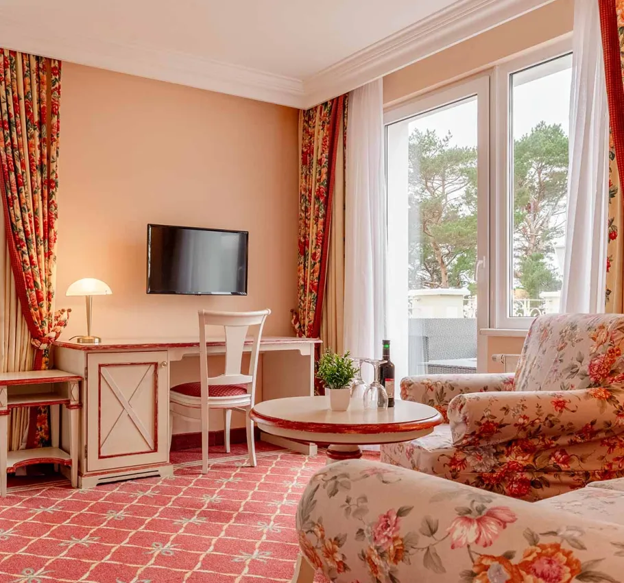 Eine gemütliche Sitzecke mit floralen Sesseln, rundem Tisch und einem Blick auf die Terrasse der Suite zur Meerseite im Rugard Strandhotel Binz.