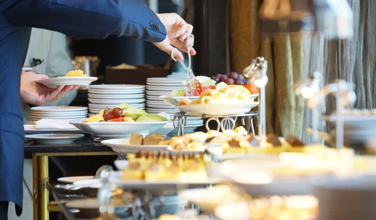 Ein Gast bedient sich am reichlich ausgestatteten Frühstücksbuffet mit Obst und Gebäck.