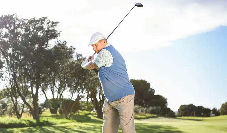 Ein Golfspieler schlägt einen Ball ab, im Hintergrund ein sonniger Golfplatz.