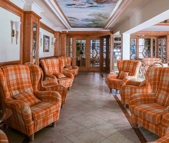Photo of the entrance area of the Rugard Thermal Strandhotel. There are orange chequered armchairs to the right and left. There is a painting on the ceiling. In the background, glass doors lead deeper into the hotel.