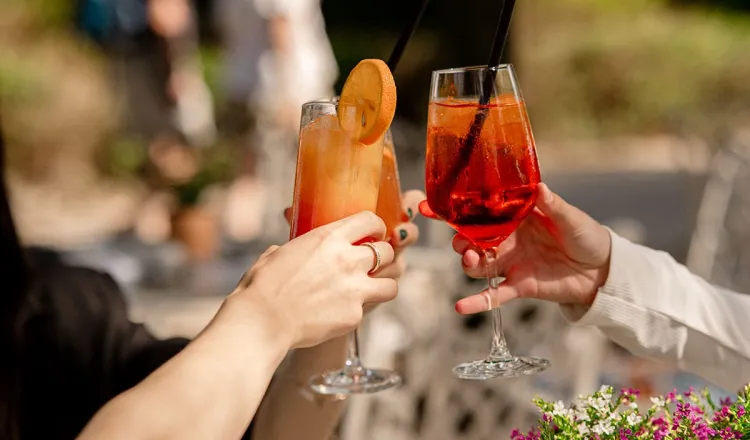 Drei Personen, von denen man nur ihre Hände sieht, stoßen mit Cocktails im Restaurant in Binz an.