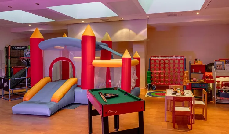 Bunter Kinderspielraum mit Hüpfburg, Kinderküche, kleinem Billardtisch, Tisch und Stühlen für kreative Beschäftigungen und vielen weiteren Utensilien für kinderfreundliche Aktivitäten.