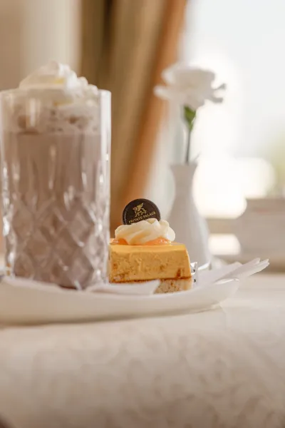Ein Stück fruchtiger Kuchen neben einem Glas heißer Schokolade mit Sahne auf einem gedeckten Tisch im Strandhotel in Binz auf Rügen.