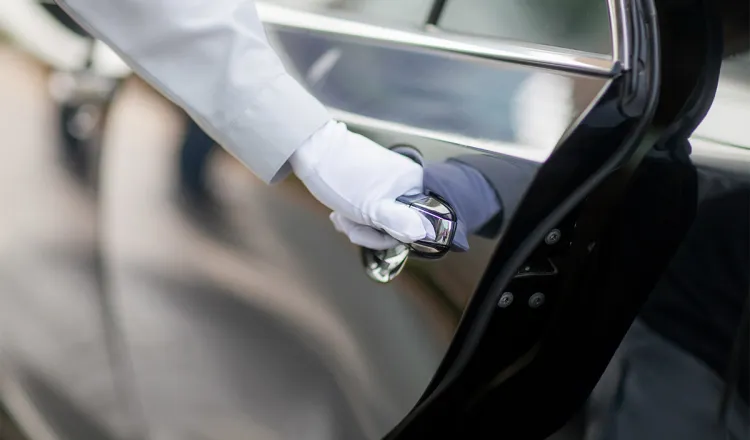Nahaufnahme der behandschuhten Hand eines Hotelangestellten beim Öffnen einer dunklen Autotür.