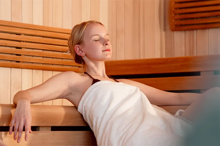 Young woman in a white towel sits with her eyes closed in the sauna at the Rugard Thermal Strandhotel.