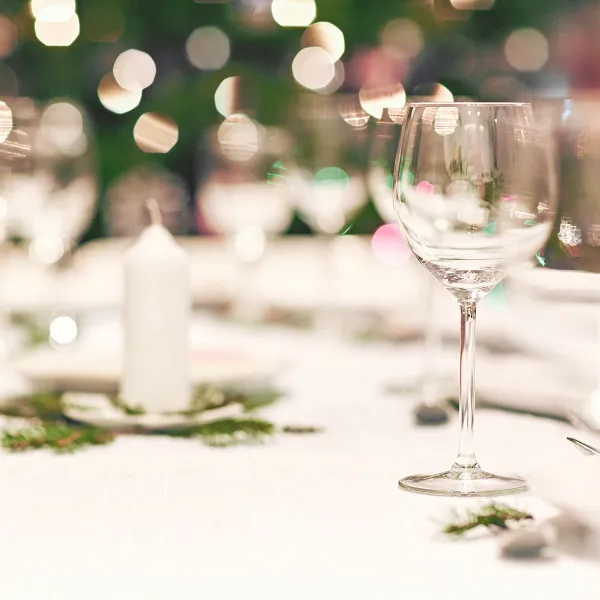 Ein leeres Glas steht auf einem weiß gedeckten Tisch mit Adventsschmuck und einer weißen Kerze bei einem Wellnessangebot auf Rügen.