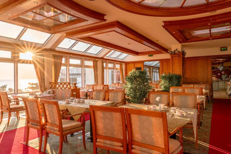 Decorated tables for up to four people in a sunlit restaurant room with a view of the Baltic Sea.