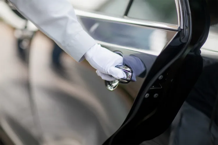 Close-up of the gloved hand of a hotel employee opening a dark car door.