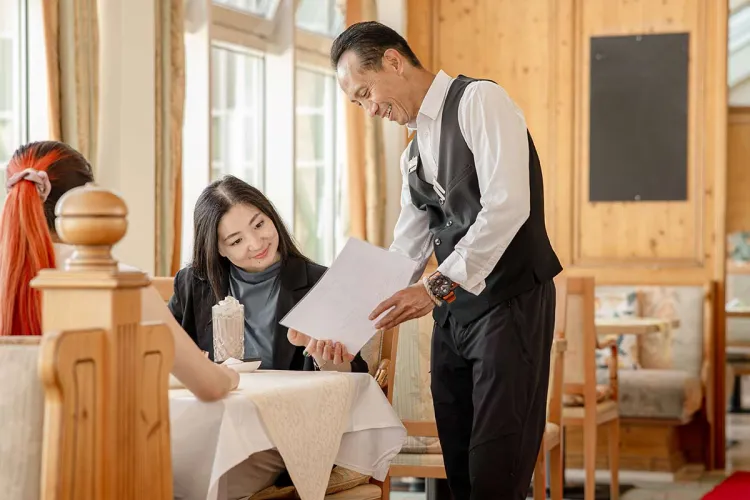 Knowledgeable Private Palace waiter explains the menu to guests – a moment of genuine hospitality.