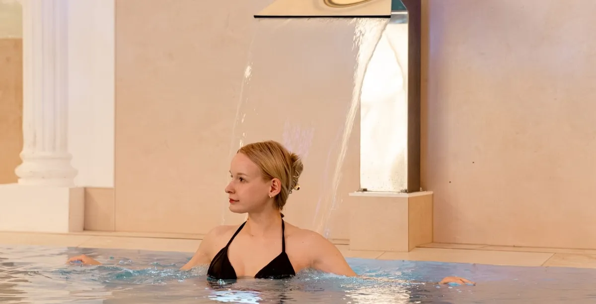 Frau entspannt im Wellnesspool mit Wasserfall im Spa-Bereich des Rugard Thermal Strandhotels in Binz.