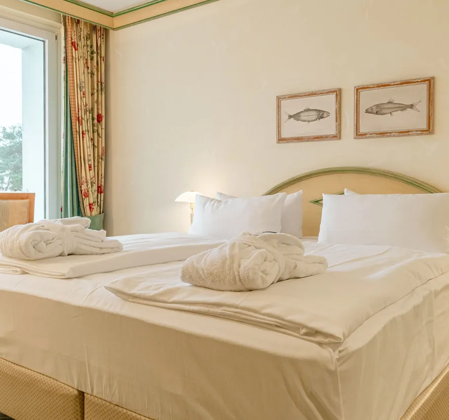Doppelbett in der Junior Suite des Rugard Strandhotels mit zwei Bademänteln und Blick aus dem Fenster auf die Ostsee
