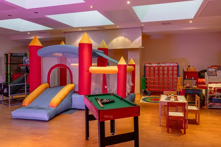 Colourful children's playroom with bouncy castle, children's kitchen, small pool table, table and chairs for creative activities and many other items for child-friendly activities.