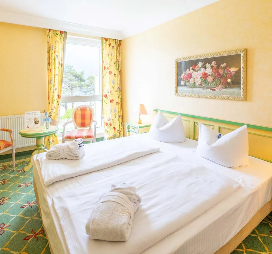 Doppelzimmer im Rugard Strandhotel Binz mit großem Bett, stilvollen Möbeln und Balkon mit Meerblick.