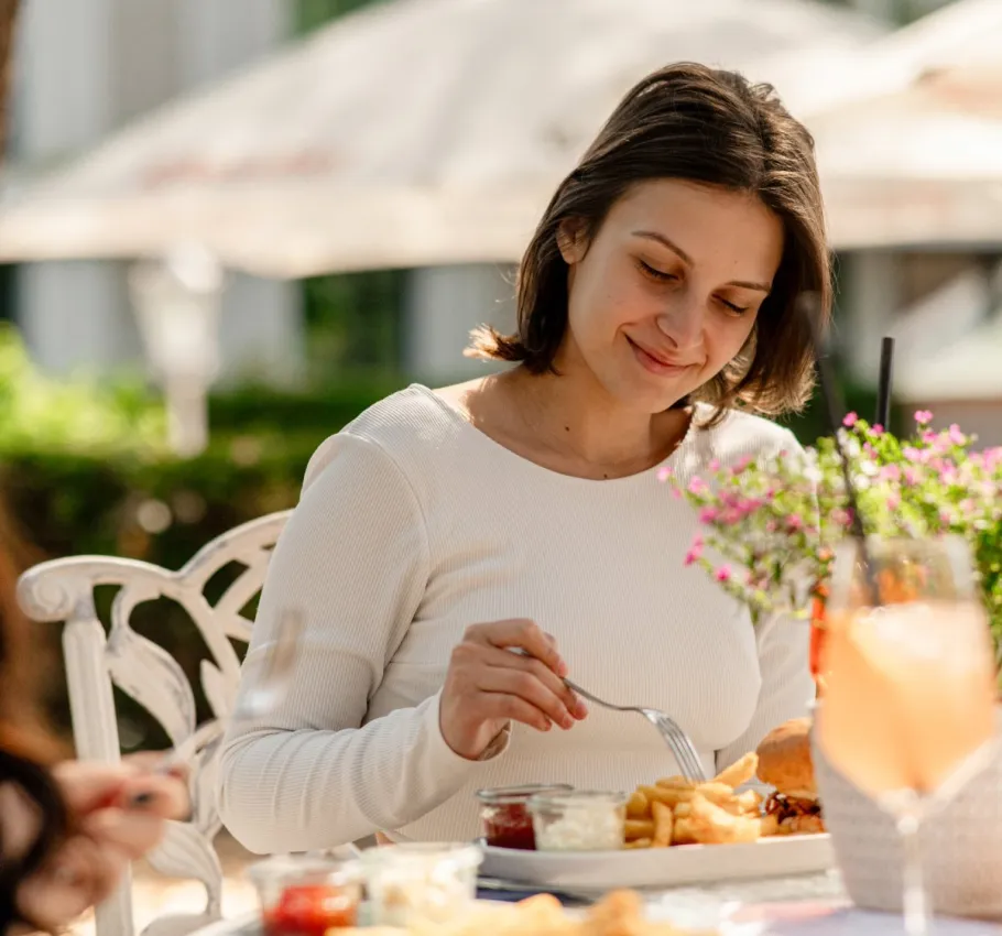 Frau genießt bei Sonnenschein ein Mittagessen mit Pommes, Burger und Getränk im Freien bei einem Wellnessangbeot auf Rügen.