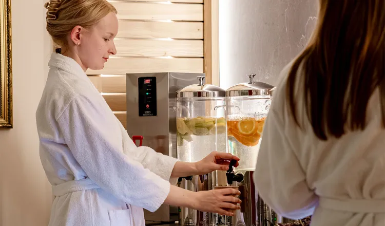 Frau im Bademantel zapft frisches Rügenwasser mit Zitrusfrüchten an der Spa-Bar des Hotel mit Sauna in Binz auf Rügen.