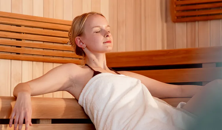 Junge Frau in weißem Handtuch sitzt mit geschlossenen Augen in der Sauna des Rugard Thermal Strandhotels in Binz.