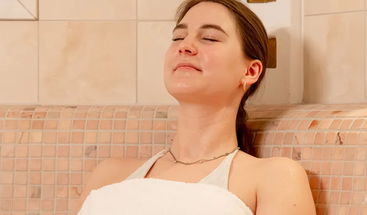 Frau lehnt entspannt mit geschlossenen Augen beim Wellness im Caldarium im Hotel mit Sauna in Binz auf Rügen.