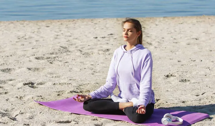 Frau meditiert beim Yoga am Strand auf Rügen mit der Ostsee im Hintergrund im Urlaub im Rugard Thermal Strandhhotel.