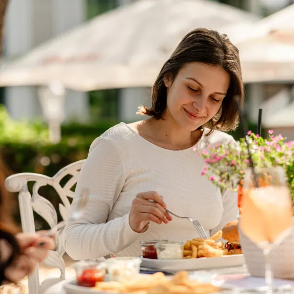 A woman enjoys lunch with fries, a burger, and a drink outdoors in the sunshine on the island of Rügen.