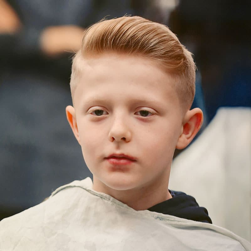 A blond boy with clothes protector, new short haircut and styling.