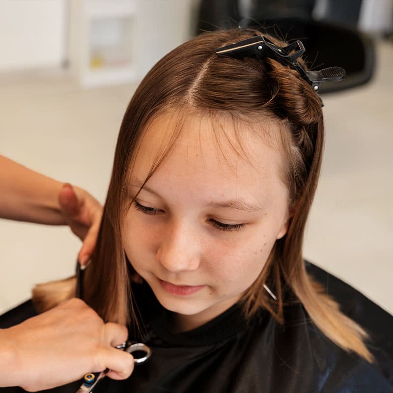 A child smiles as he watches his new hair length being measured with a comb.