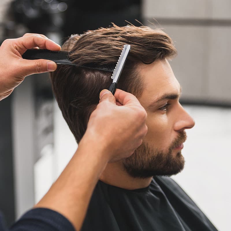 Dark-blonde man gets loose short hairstyle with comb and razor.