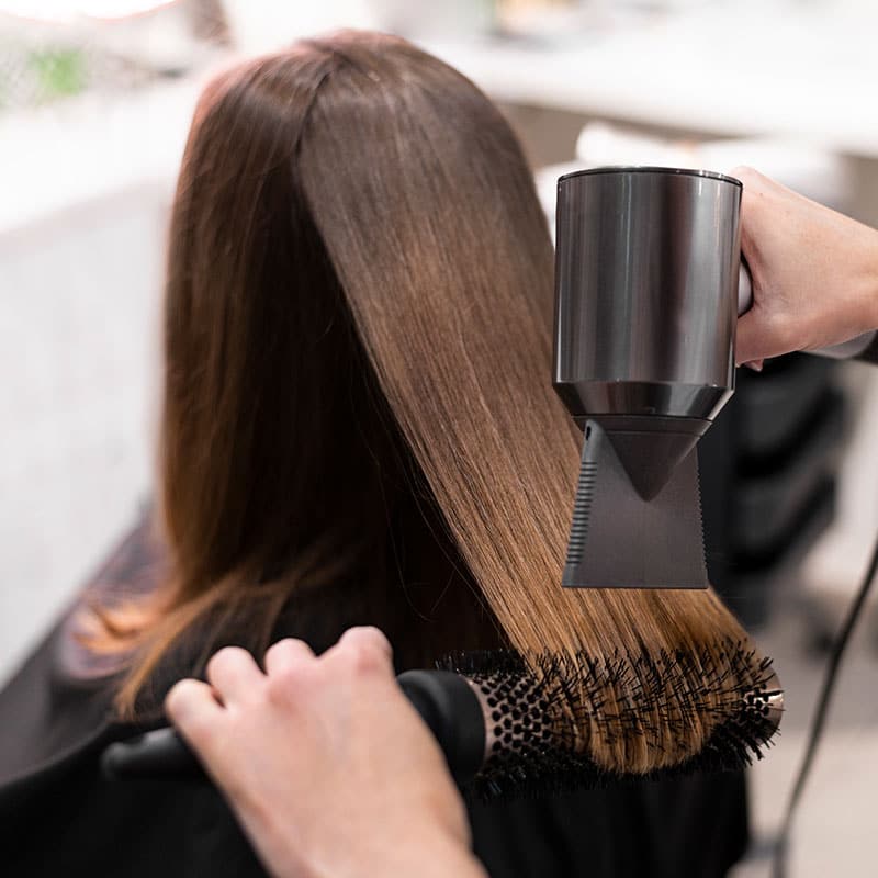 Brunette person receives a professional blow-dry treatment for her shoulder-length hair.
