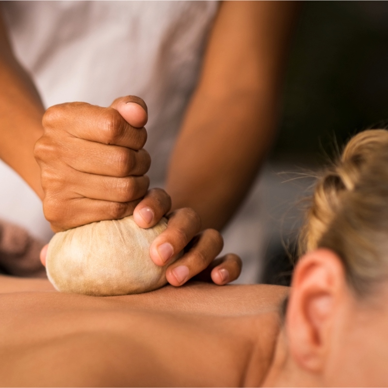 Close-up of a woman receiving a soothing Ayurvedic herbal stamp massage on her back.