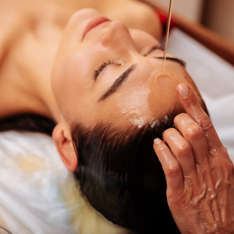 Close-up of a woman having oil poured on her head for a massage.