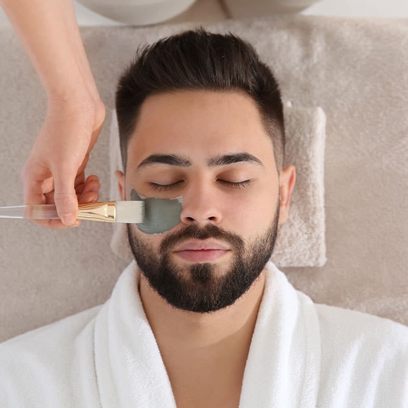 Man relaxes while receiving a cleansing face mask.