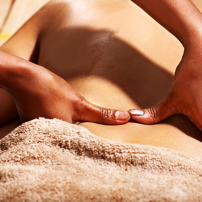 Close-up of the hands of a wellness employee performing a full-body massage with aromatic oil while massaging the back.