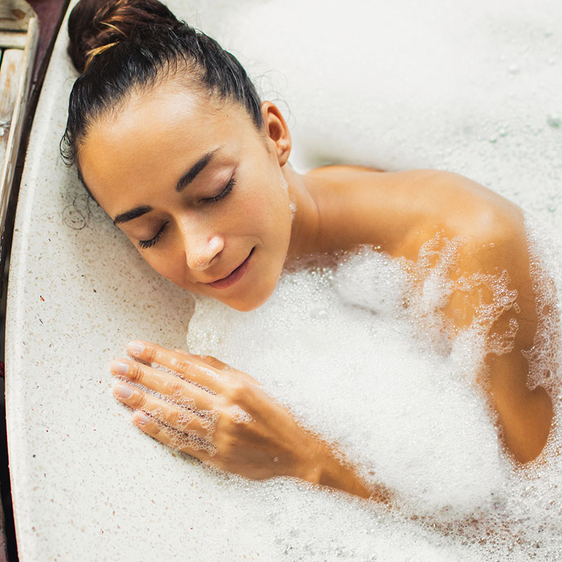 A dark-haired woman takes an aromatic oil bath and closes her eyes while relaxing.