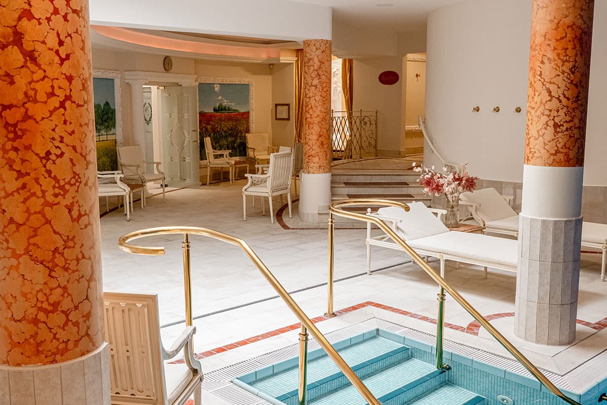 Poolbereich im Rugard Thermal Strandhotel im antiken Bäder-Stil mit Säulen und goldenen Handläufen.