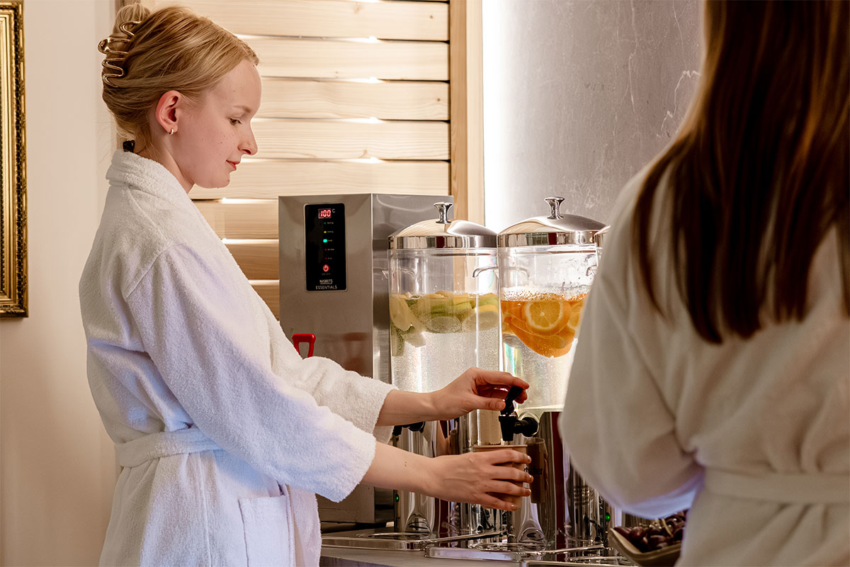 Frau im Bademantel zapft frisches Rügenwasser mit Zitrusfrüchten an der Spa-Bar des Hotel mit Sauna in Binz auf Rügen.