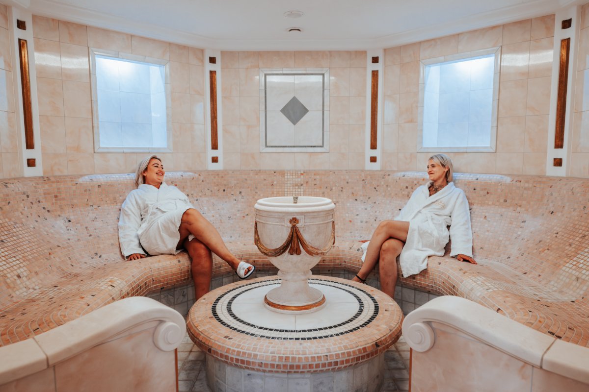 Zwei Frauen sitzen im Caldarium im Hotel mit Sauna in Binz auf Rügen auf beheizten Steinbänken mit Mosaikverkleidung.
