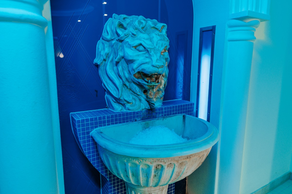 Löwenkopf mit Eisbrunnen unter blauer Beleuchtung, Teil des Wellnessbereichs im Hotel mit Sauna in Binz auf Rügen.