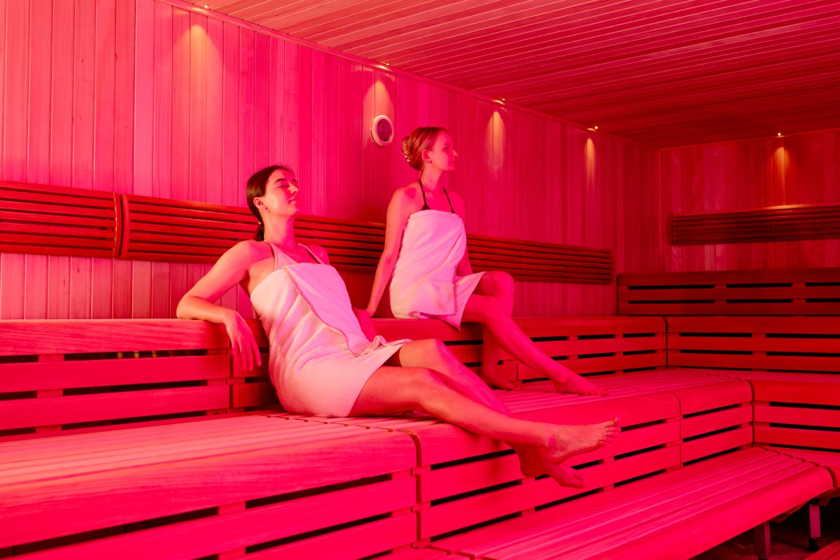 Zwei Frauen sitzen in der rot beleuchteten finnischen Sauna des Rugard Thermal Strandhotels in Binz.